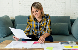 Woman with blonde hair in plaid shirt reviews credit documents on a teal sofa