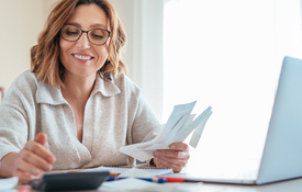 woman with a soft smile and glasses evaluating her expenses in a well-lit room