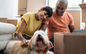 A mixed race couple and their dog smile as they unpack. 