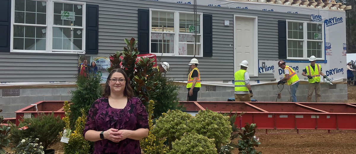 A woman stands in front of her under construction home with plants 