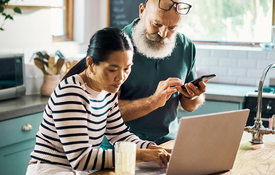 Mixed race couple reviews paperwork on their laptop in the kitchen